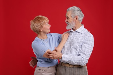 Photo of Lovely senior couple looking at each other on red background