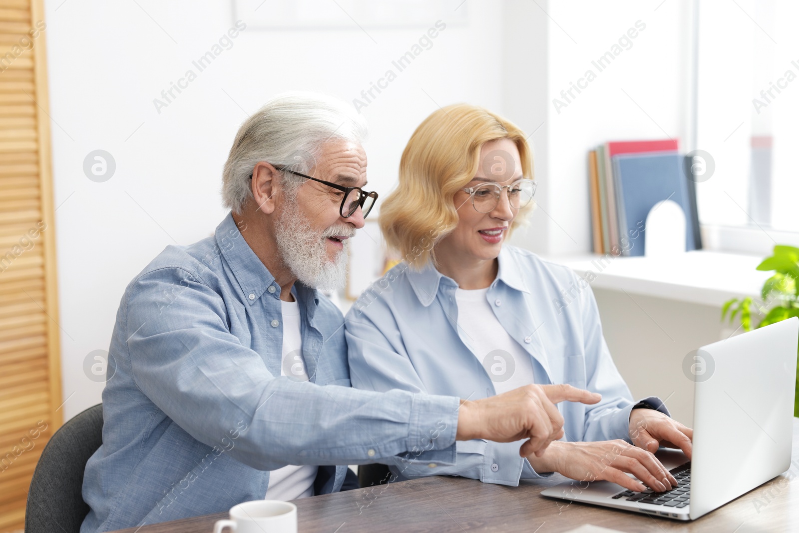 Photo of Senior man and mature woman watching something on laptop at home. Happy couple