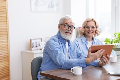 Photo of Senior man and mature woman watching something on tablet at home. Happy couple