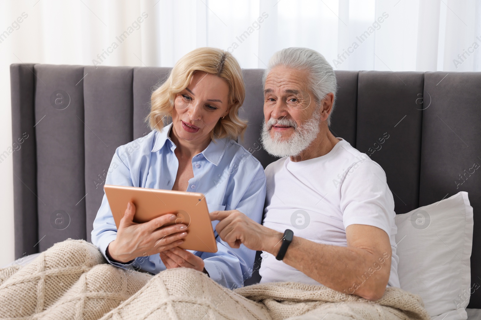 Photo of Senior man and mature woman with tablet spending time together at home. Happy couple