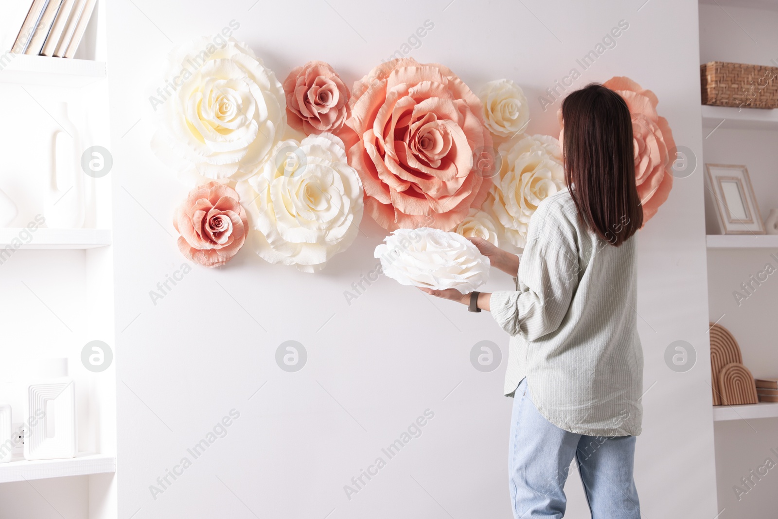 Photo of Woman decorating wall with beautiful paper flowers at home, back view