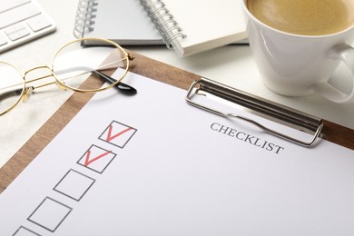 Photo of Checklist with marked checkboxes, stationery, glasses and coffee on white table, closeup