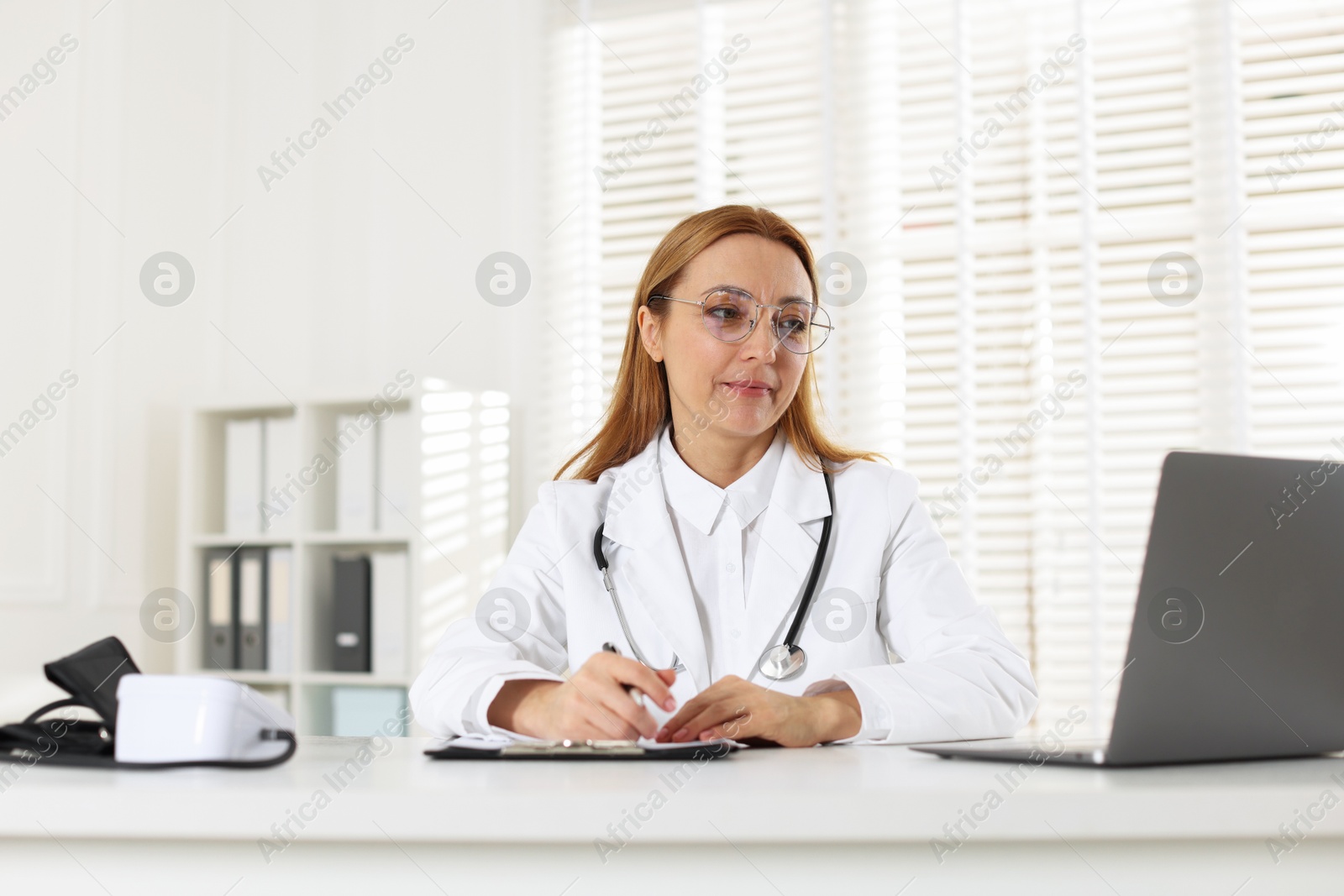 Photo of Cardiologist with stethoscope working at white table in clinic