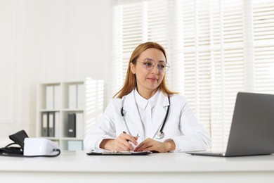 Photo of Cardiologist with stethoscope working at white table in clinic