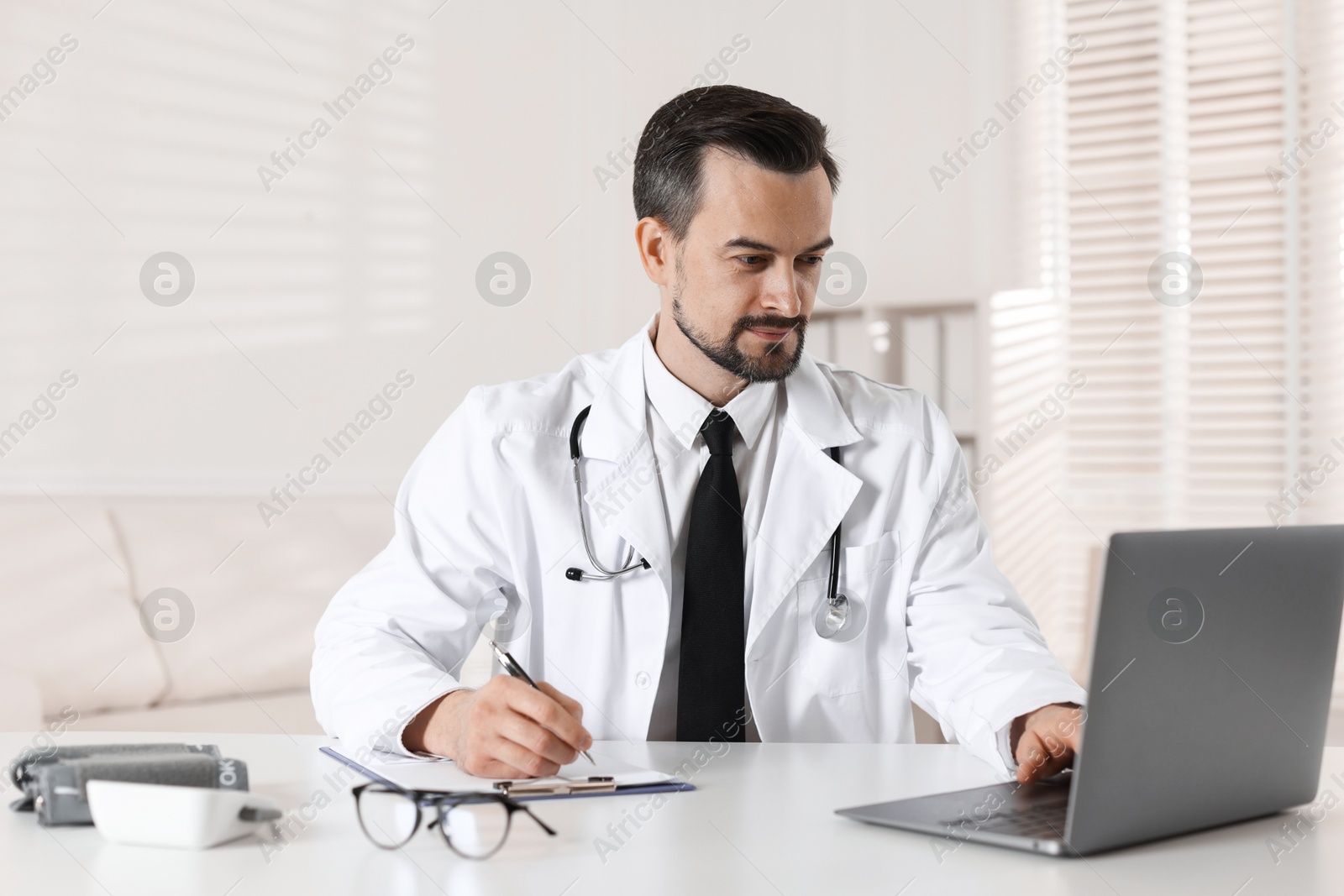 Photo of Cardiologist with stethoscope working at white table in clinic