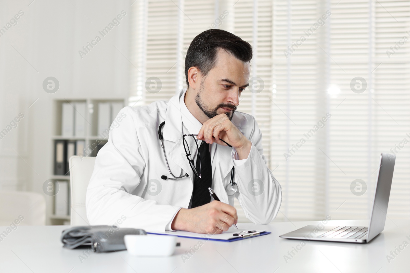 Photo of Cardiologist with stethoscope working at white table in clinic