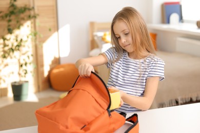 Photo of Girl packing lunch box into backpack at home