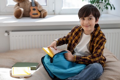 Photo of Boy packing backpack for school on bed at home