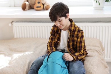 Photo of Boy packing backpack for school on bed at home, space for text