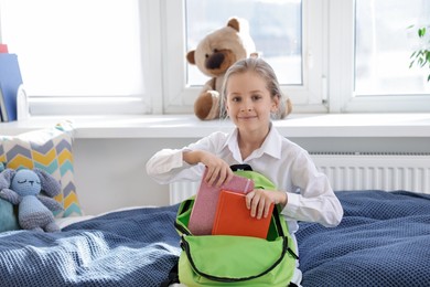 Photo of Girl packing backpack for school on bed at home