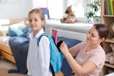 Photo of Mother helping her daughter packing backpack for school at home