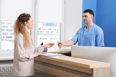 Photo of Patient giving medical insurance card to smiling receptionist in clinic