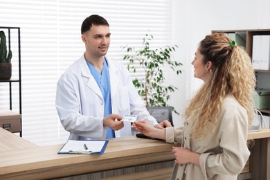 Photo of Patient giving medical insurance card to smiling receptionist at counter in clinic