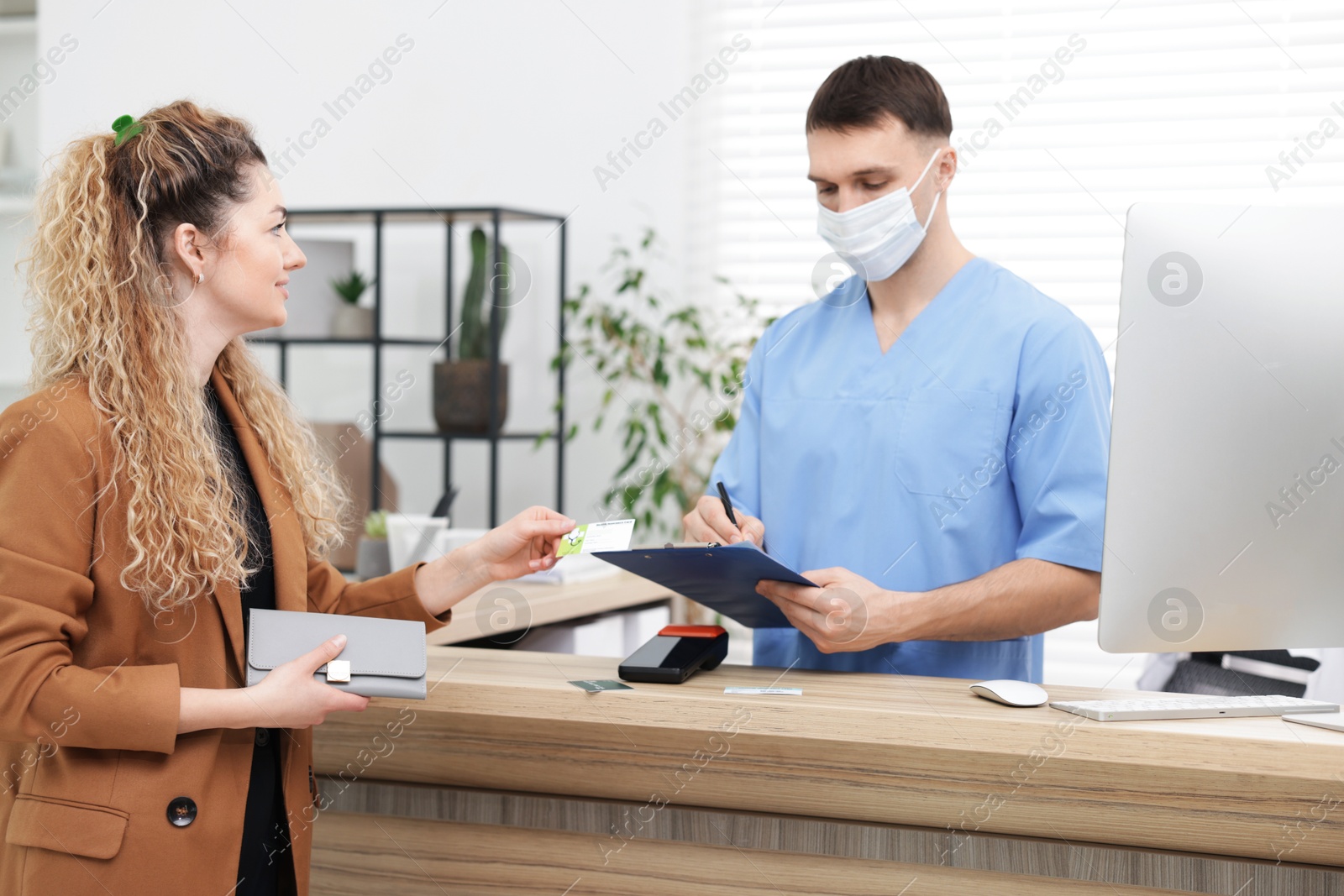 Photo of Patient with medical insurance card and receptionist filling document at counter in clinic