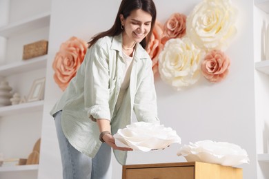 Photo of Woman decorating wall with beautiful paper flowers at home, low angle view