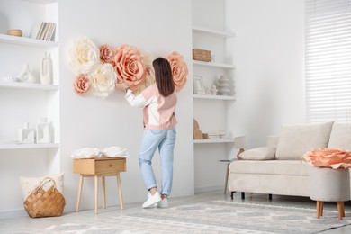 Photo of Woman decorating wall with beautiful paper flowers at home