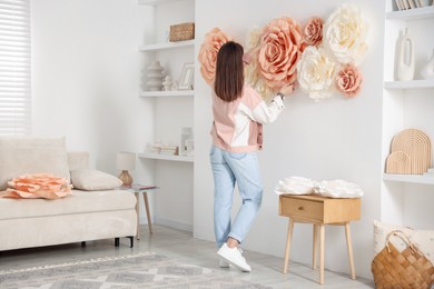 Photo of Woman decorating wall with beautiful paper flowers at home