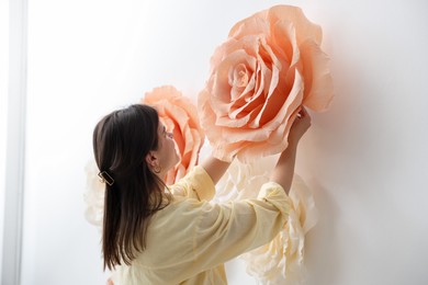 Photo of Woman decorating wall with beautiful paper flowers at home