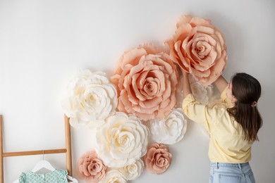 Photo of Woman decorating wall with beautiful paper flowers at home, back view