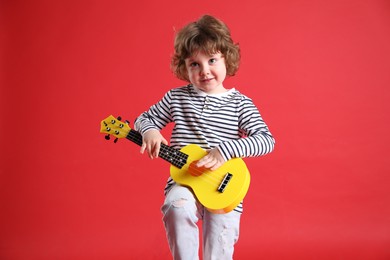 Photo of Cute little boy playing toy guitar on red background