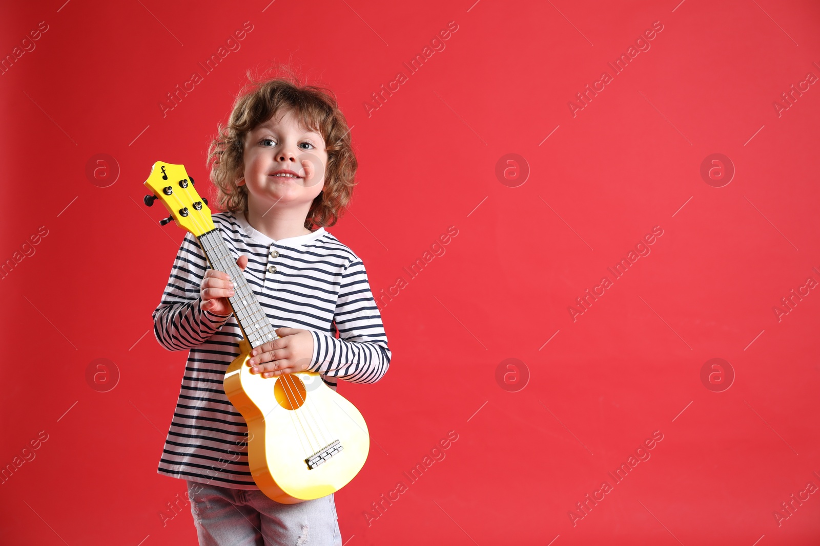 Photo of Cute little boy playing toy guitar on red background. Space for text