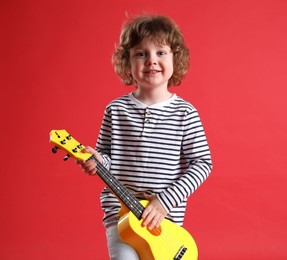 Photo of Cute little boy playing toy guitar on red background