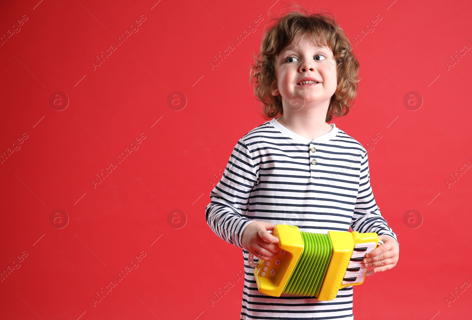 Photo of Cute little boy playing toy accordion on red background. Space for text