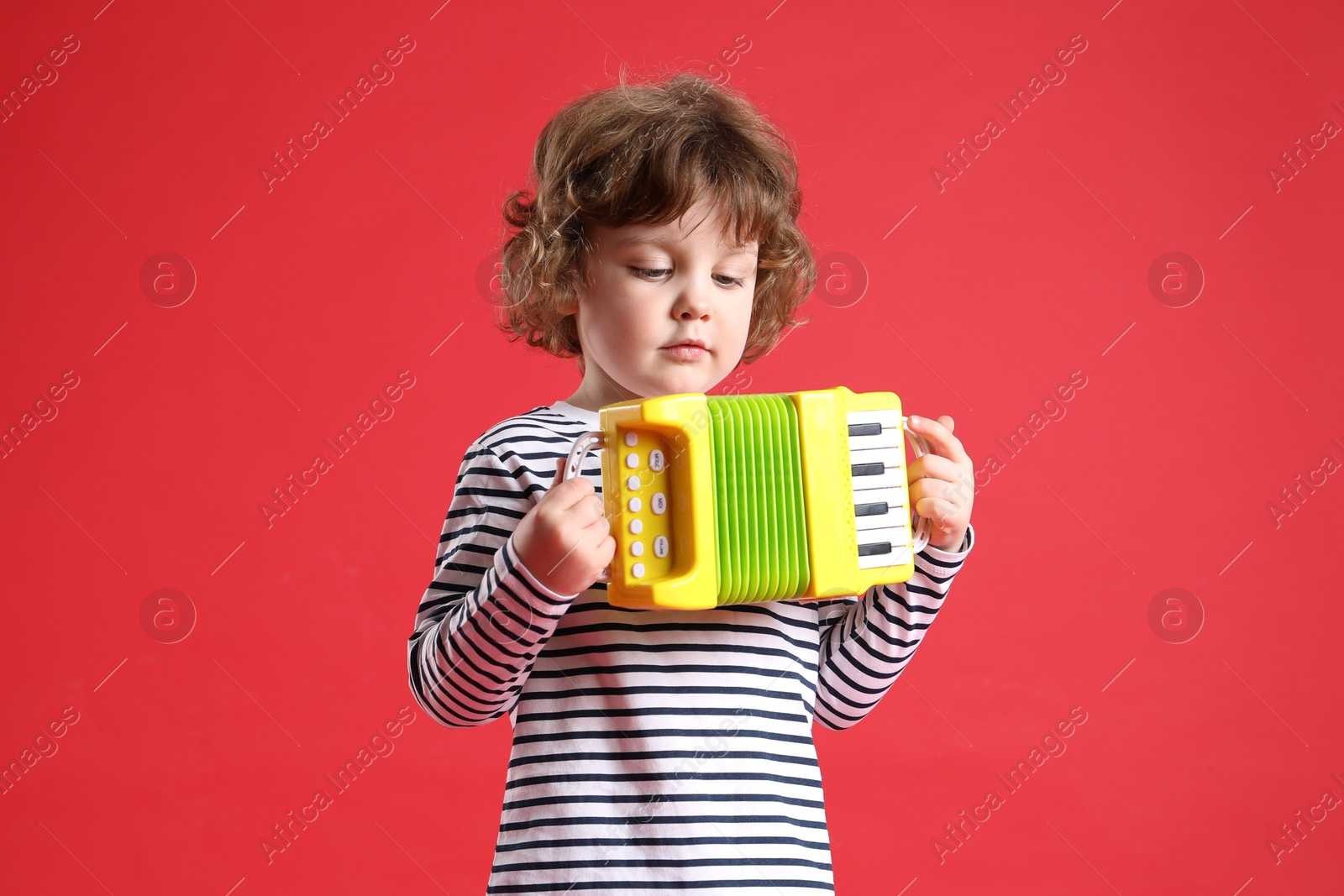 Photo of Cute little boy playing toy accordion on red background