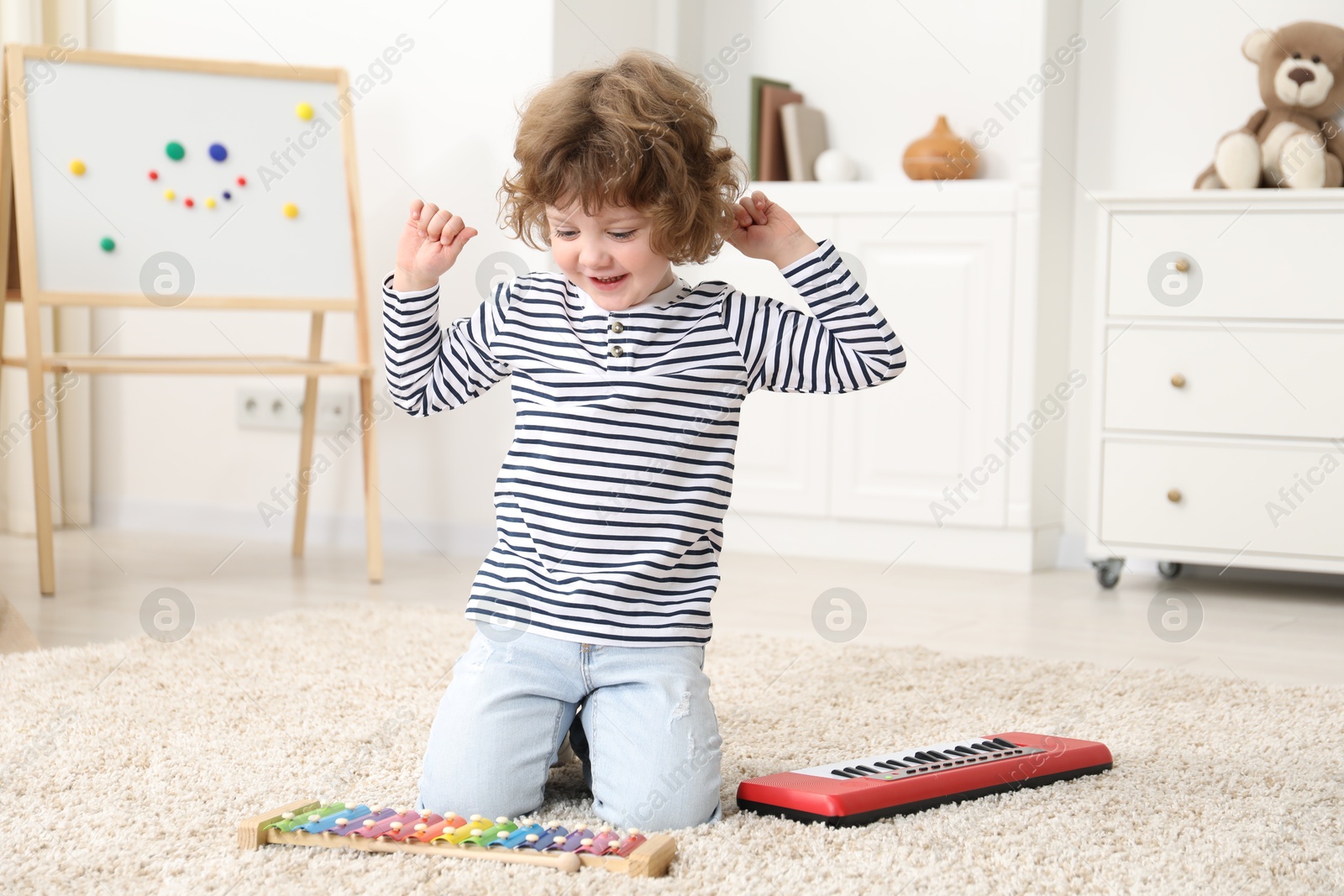 Photo of Cute little boy playing toy musical instruments on floor at home