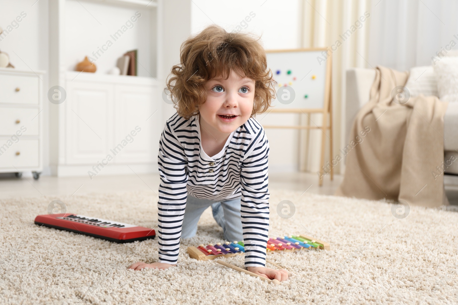 Photo of Cute little boy playing toy musical instruments on floor at home