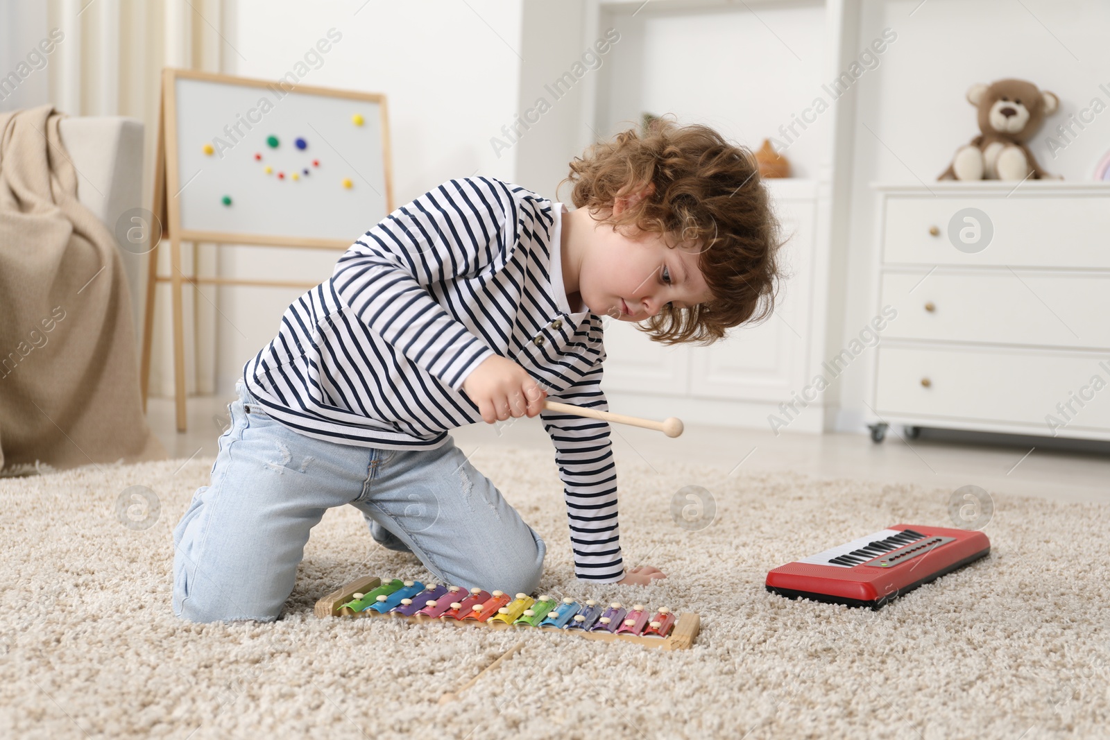 Photo of Cute little boy playing toy xylophone on floor at home