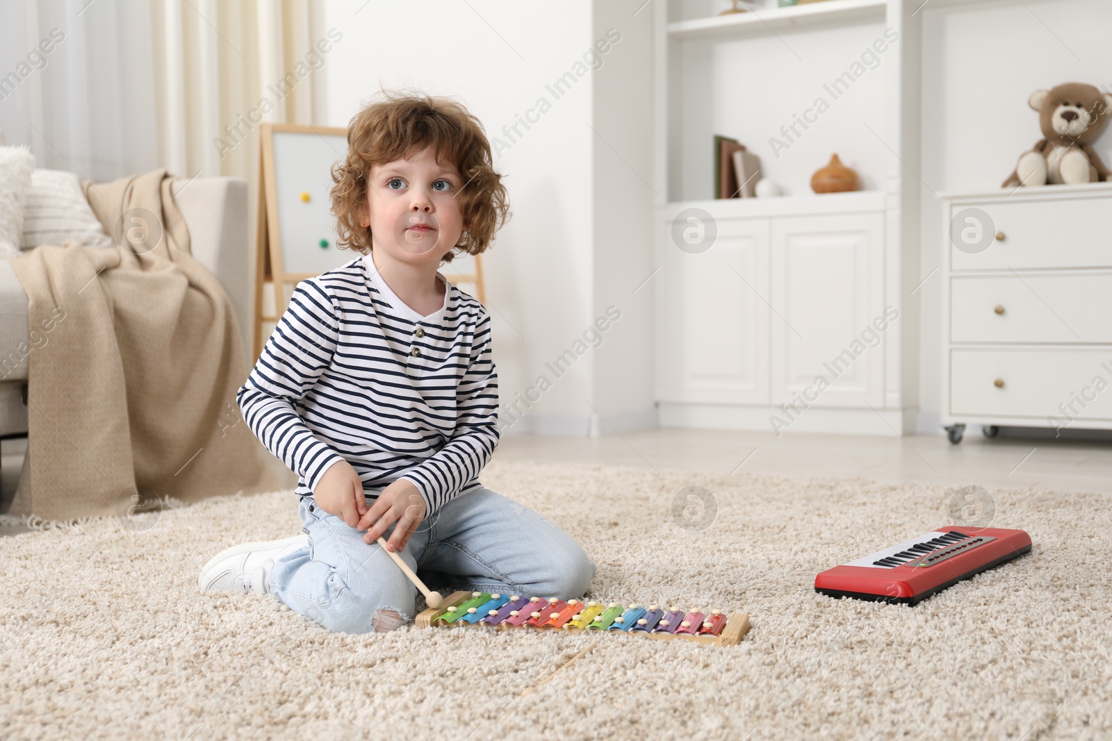 Photo of Cute little boy playing toy xylophone on floor at home. Space for text