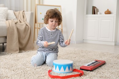 Photo of Cute little boy playing toy drum on floor at home. Space for text