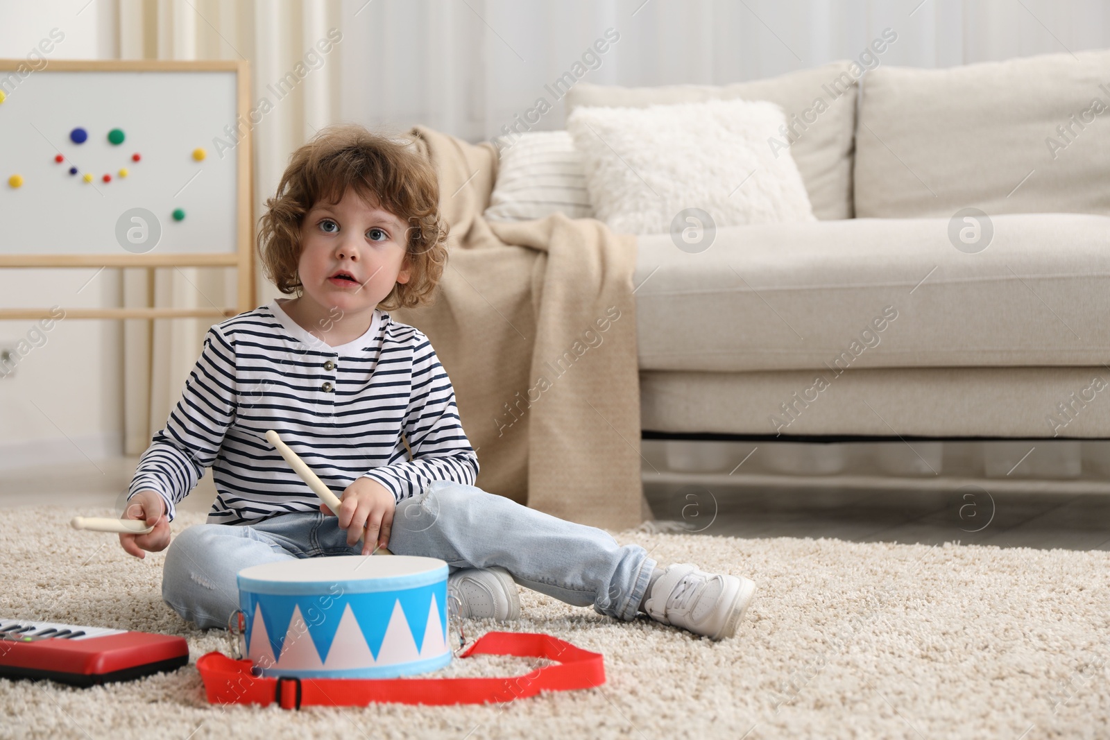 Photo of Cute little boy playing toy drum on floor at home. Space for text