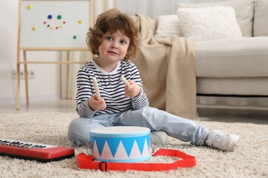 Photo of Cute little boy playing toy drum on floor at home