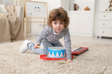 Photo of Cute little boy playing toy drum on floor at home