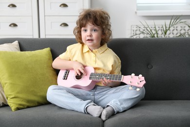 Photo of Cute little boy playing toy guitar on sofa at home