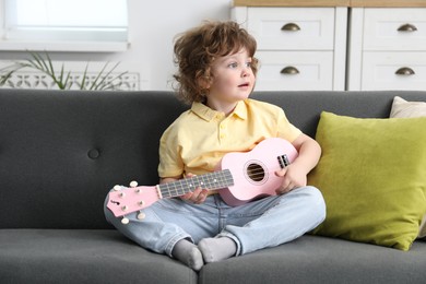 Photo of Cute little boy playing toy guitar on sofa at home