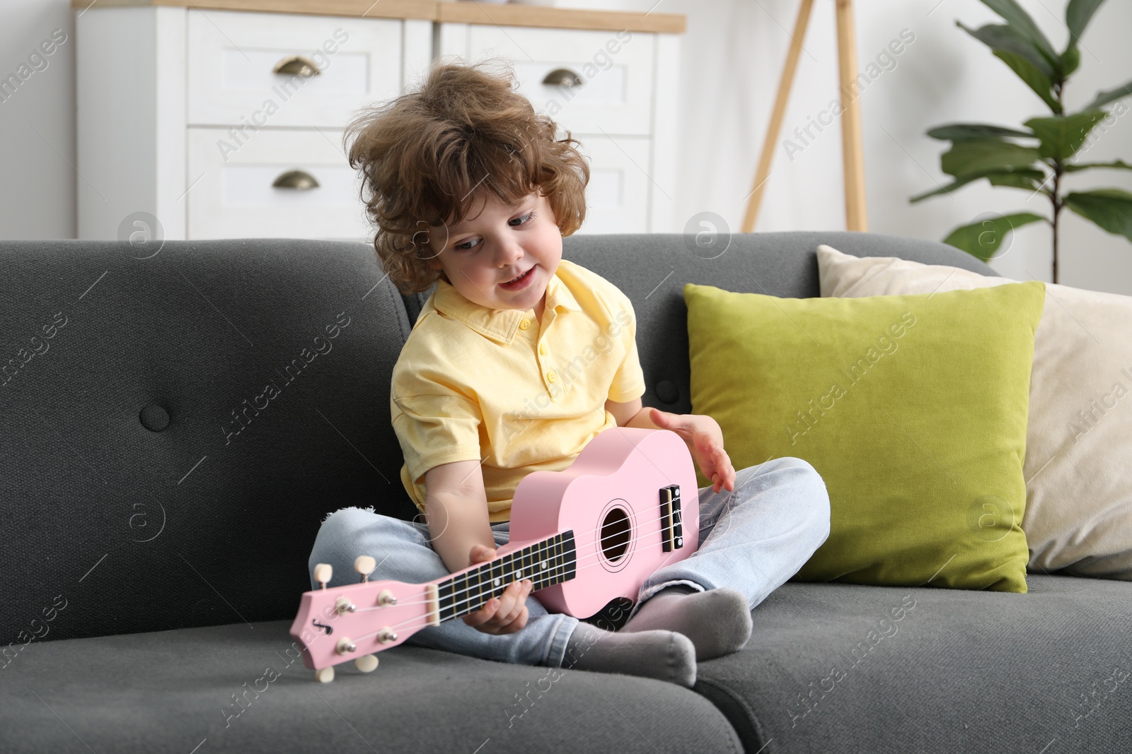 Photo of Cute little boy playing toy guitar on sofa at home