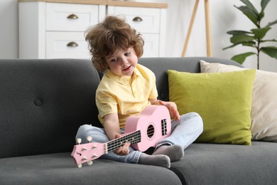 Photo of Cute little boy playing toy guitar on sofa at home