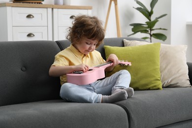 Photo of Cute little boy playing toy guitar on sofa at home