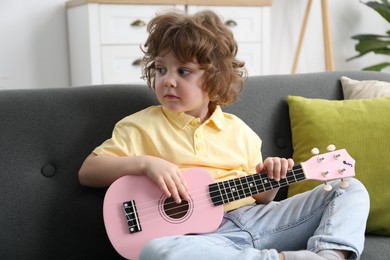 Photo of Cute little boy playing toy guitar on sofa at home