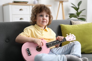 Photo of Cute little boy playing toy guitar on sofa at home