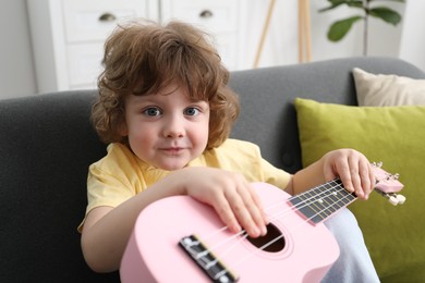 Photo of Cute little boy playing toy guitar on sofa at home