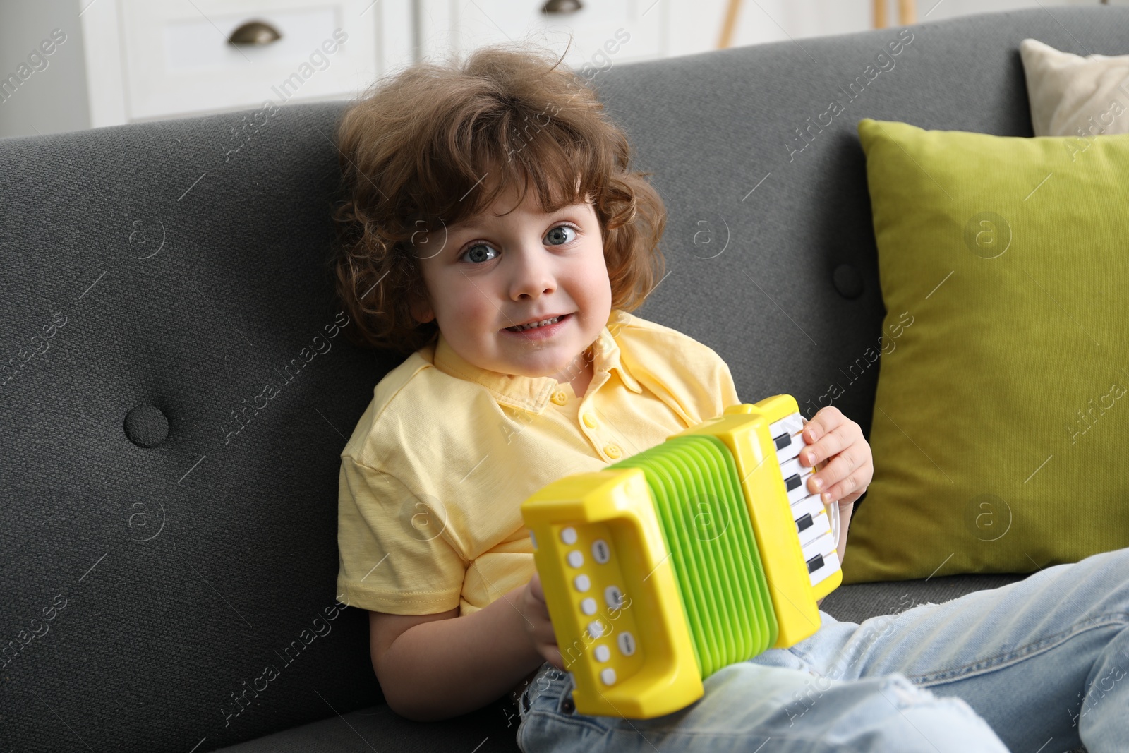 Photo of Cute little boy playing toy accordion on sofa at home