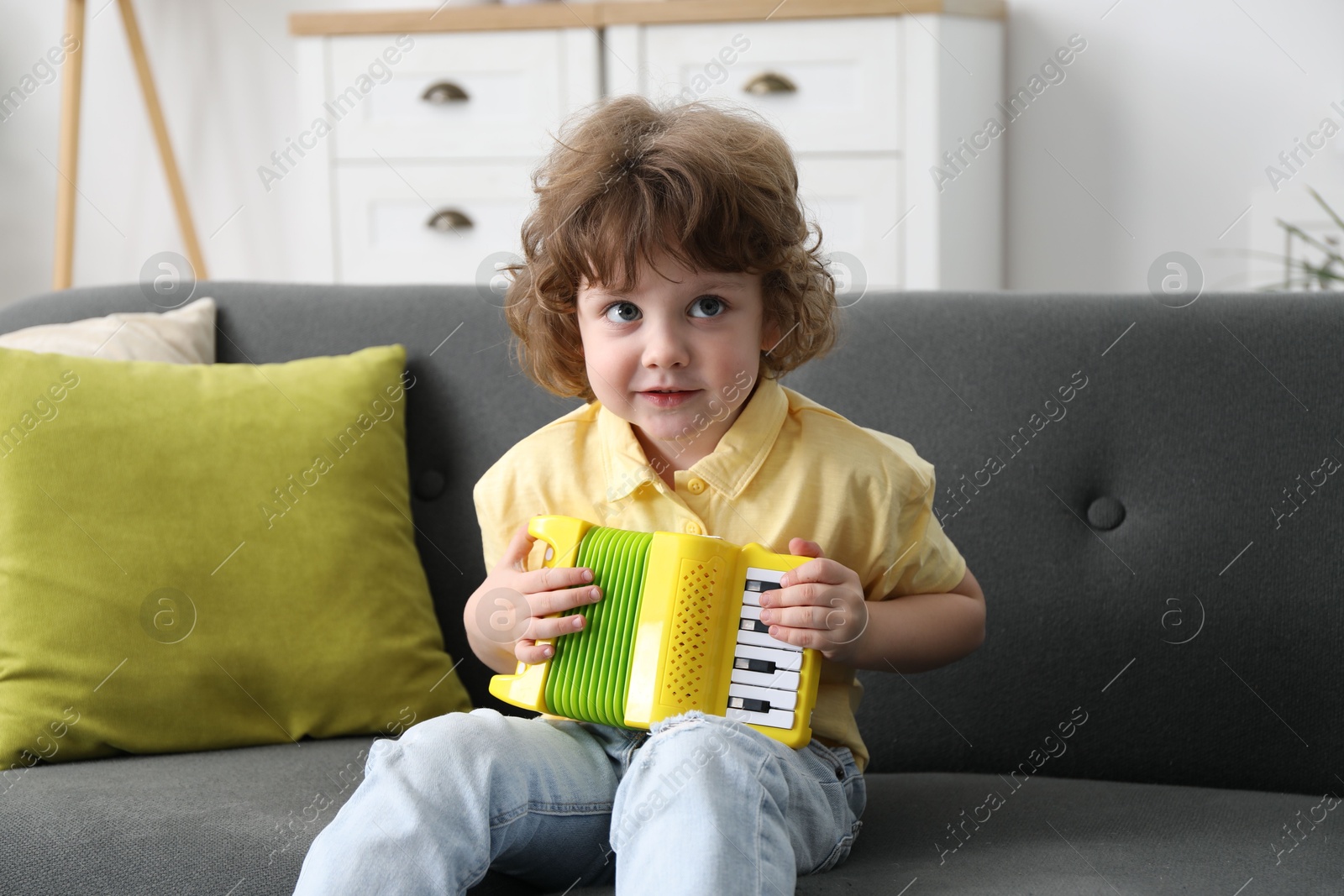 Photo of Cute little boy playing toy accordion on sofa at home