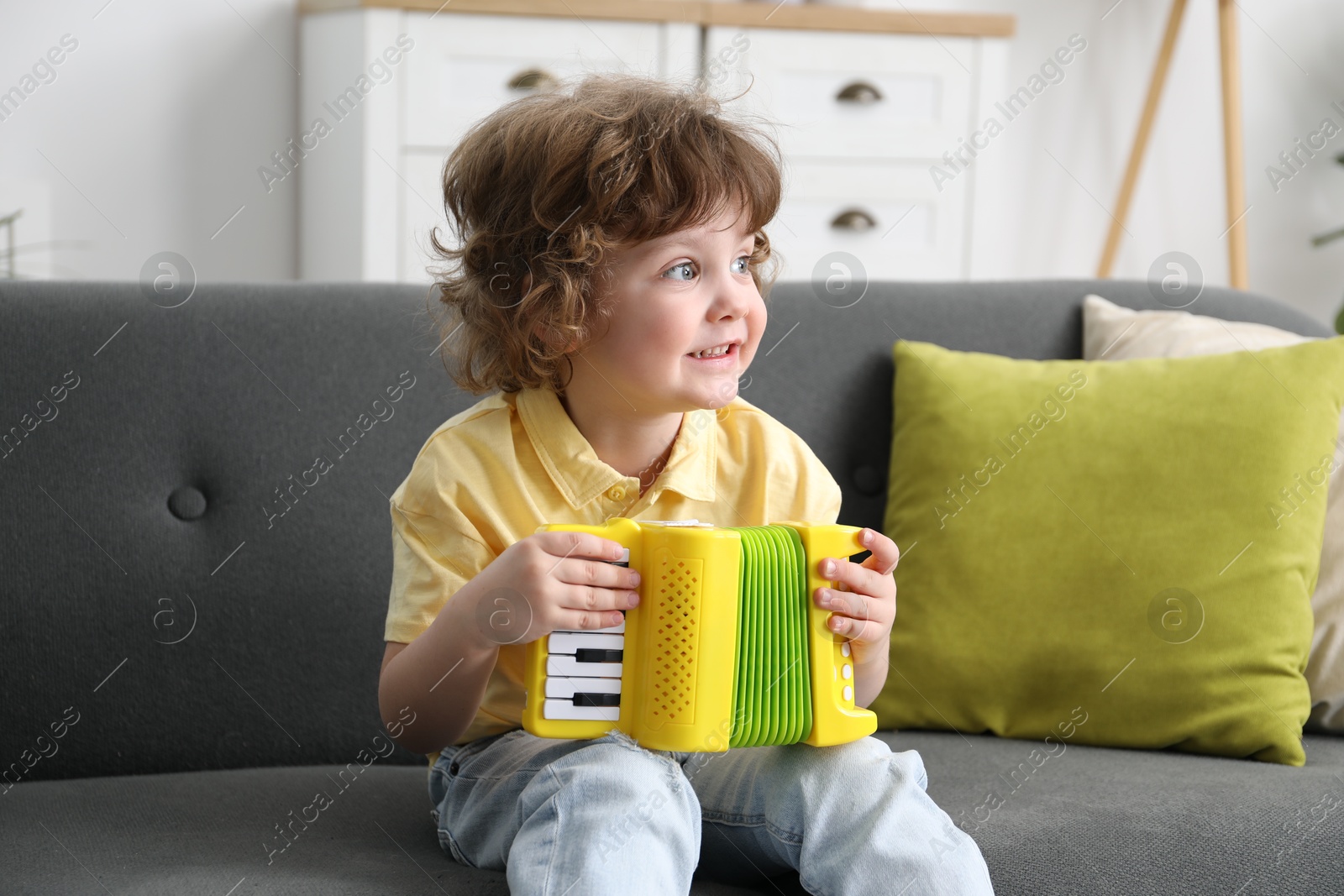 Photo of Cute little boy playing toy accordion on sofa at home