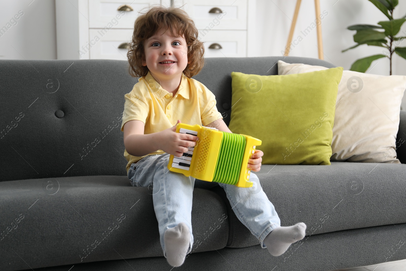 Photo of Cute little boy playing toy accordion on sofa at home