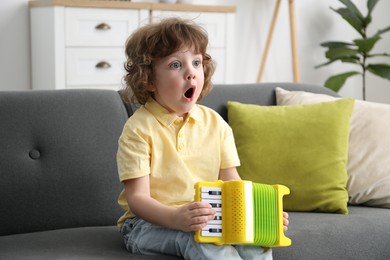 Photo of Cute little boy playing toy accordion on sofa at home