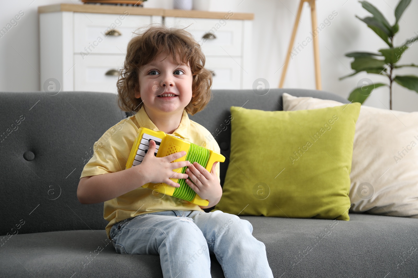 Photo of Cute little boy playing toy accordion on sofa at home